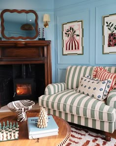 a living room with blue walls and striped furniture in front of a fire place that has chess pieces on the coffee table