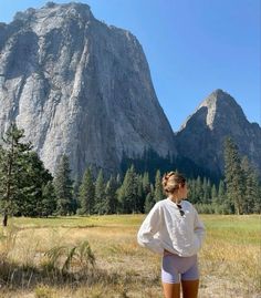 a woman standing in front of a mountain with her back to the camera, wearing white shorts