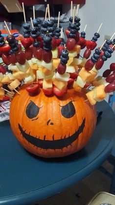 a carved pumpkin with fruit on it's head sitting on top of a table