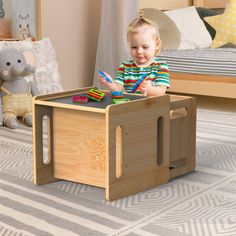 a small child playing with toys in a wooden box on the floor next to a bed