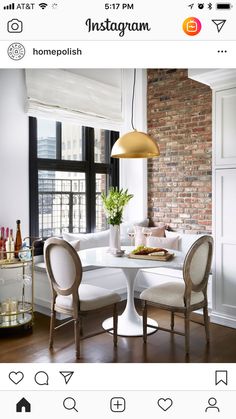 a dining room with brick walls and white furniture, along with a round table surrounded by beige upholstered chairs