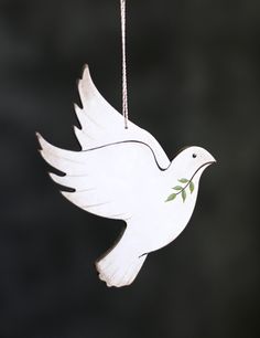 a white dove ornament hanging from a chain on a black background with green leaves