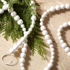 a white beaded necklace and ring sitting on top of a marble surface next to a pine tree