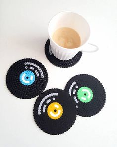 three coasters with smiley faces on them next to a cup of coffee