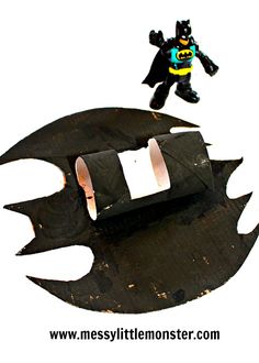 a lego batman figure standing on top of a black bat shaped object with holes in it