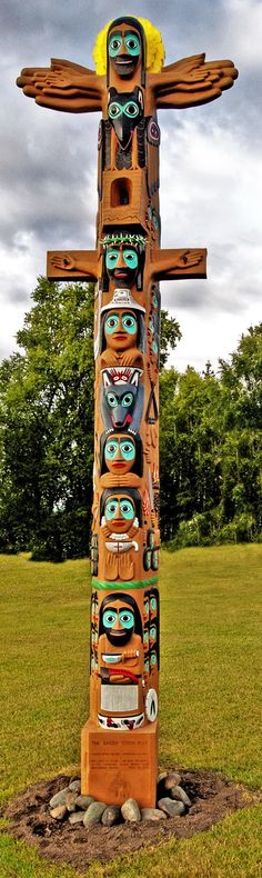 a totem pole in the middle of a field with many faces painted on it