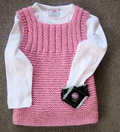 a pink and white sweater sitting on top of a carpet next to a black purse