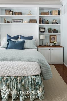 a bed with blue and white pillows in a bedroom next to a book shelf filled with books