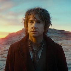 a young man standing in front of a mountain with the sun setting on it's horizon