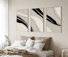 two paintings hang above a bed in a room with white walls and pillows on it