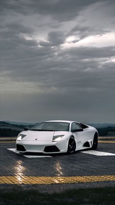 a white sports car is parked on the tarmac at dusk with dark clouds in the background