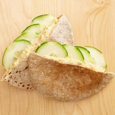 a sandwich with cucumber slices cut in half on top of a wooden table