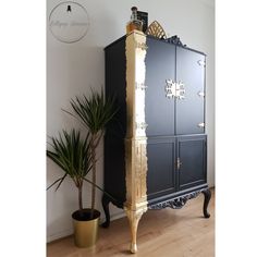 a tall black cabinet with gold trimmings and two potted plants next to it