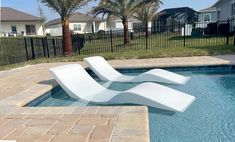 two white lounge chairs sitting next to a swimming pool with palm trees in the background