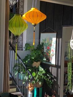 three lanterns hanging from the side of a stair case filled with potted plants and greenery