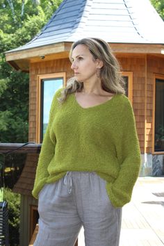 a woman standing in front of a wooden structure wearing a green sweater and grey pants