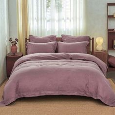 a bed with purple sheets and pillows in a room next to a book shelf filled with books