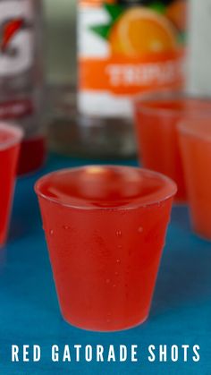 red gatorade shots are lined up on a blue table with oranges in the background