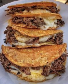 three tacos stacked on top of each other in a white plate with meat and cheese