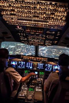 two pilots are sitting in the cockpit of an airplane at night, with lights on