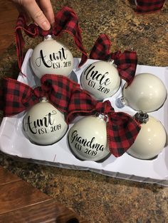 christmas ornaments with red and black plaid ribbon tied around them in a white box on a table