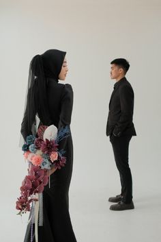 a man standing next to a woman wearing a black dress and holding a flower bouquet