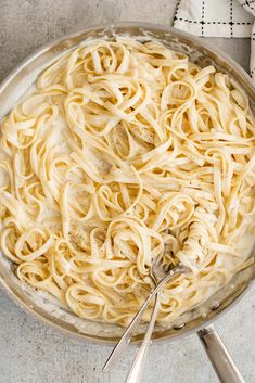 a pan filled with pasta and sauce on top of a table next to utensils