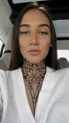 a woman with tattoos on her neck sitting in the back seat of a car and looking at the camera