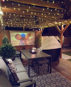 a patio with lights strung from the ceiling and an outdoor movie screen on the wall