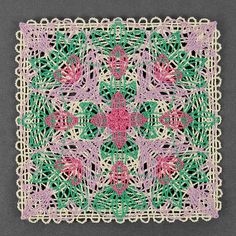 a crocheted doily with pink flowers and green leaves on it, against a gray background