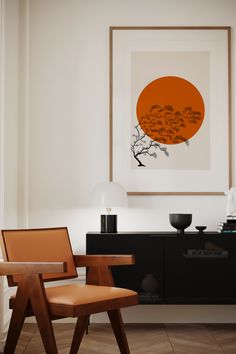 an orange and black art piece hangs above a chair in a room with white walls