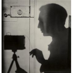 a black and white photo of a person holding a camera in front of a door