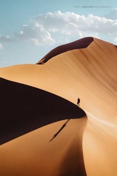 a person standing on top of a large sand dune in the middle of the desert