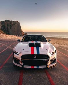 a white sports car parked on top of a parking lot next to the ocean at sunset