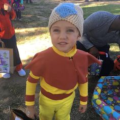 a young boy wearing a costume standing next to other children in the grass and trees