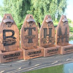 four wooden plaques with the names of three different businesses on them, along with a pond and trees in the background