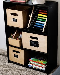 a black bookcase with three bins on top of it and some books in the bottom drawer