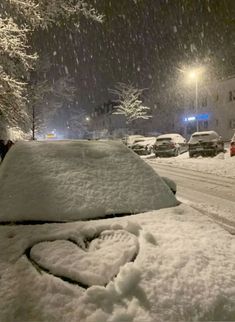 cars parked on the side of a snowy road at night with snow falling all around