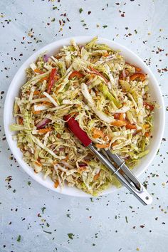 a white bowl filled with coleslaw and carrots next to two tongs