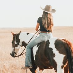 a woman riding on the back of a brown and white horse in a dry grass field