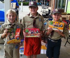 three boys in scout uniforms holding packages of cereal