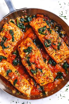 salmon with tomato sauce and spinach in a skillet on a white counter top