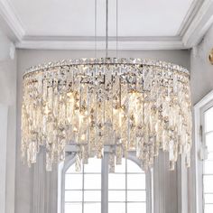 a crystal chandelier hanging from the ceiling in a living room with large windows