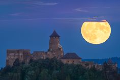 the full moon is setting over an old castle