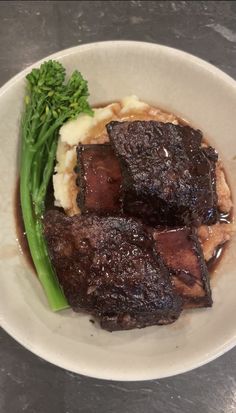 a white plate topped with meat and mashed potatoes next to broccoli on top of a table