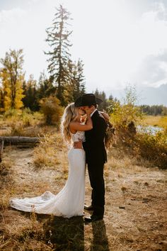 a bride and groom kissing in the middle of an open field surrounded by tall trees