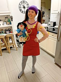 a woman is standing in the kitchen with her hands on her hips and holding two dolls