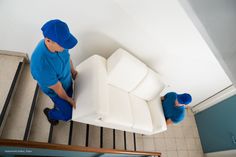 a man in blue jumpsuits working on a white couch next to some stairs