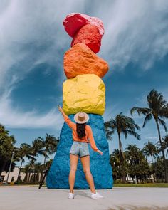 a woman standing in front of a giant rock with five different colored rocks on it