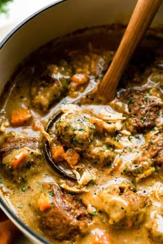 a pot filled with meatballs and vegetables in gravy next to a wooden spoon